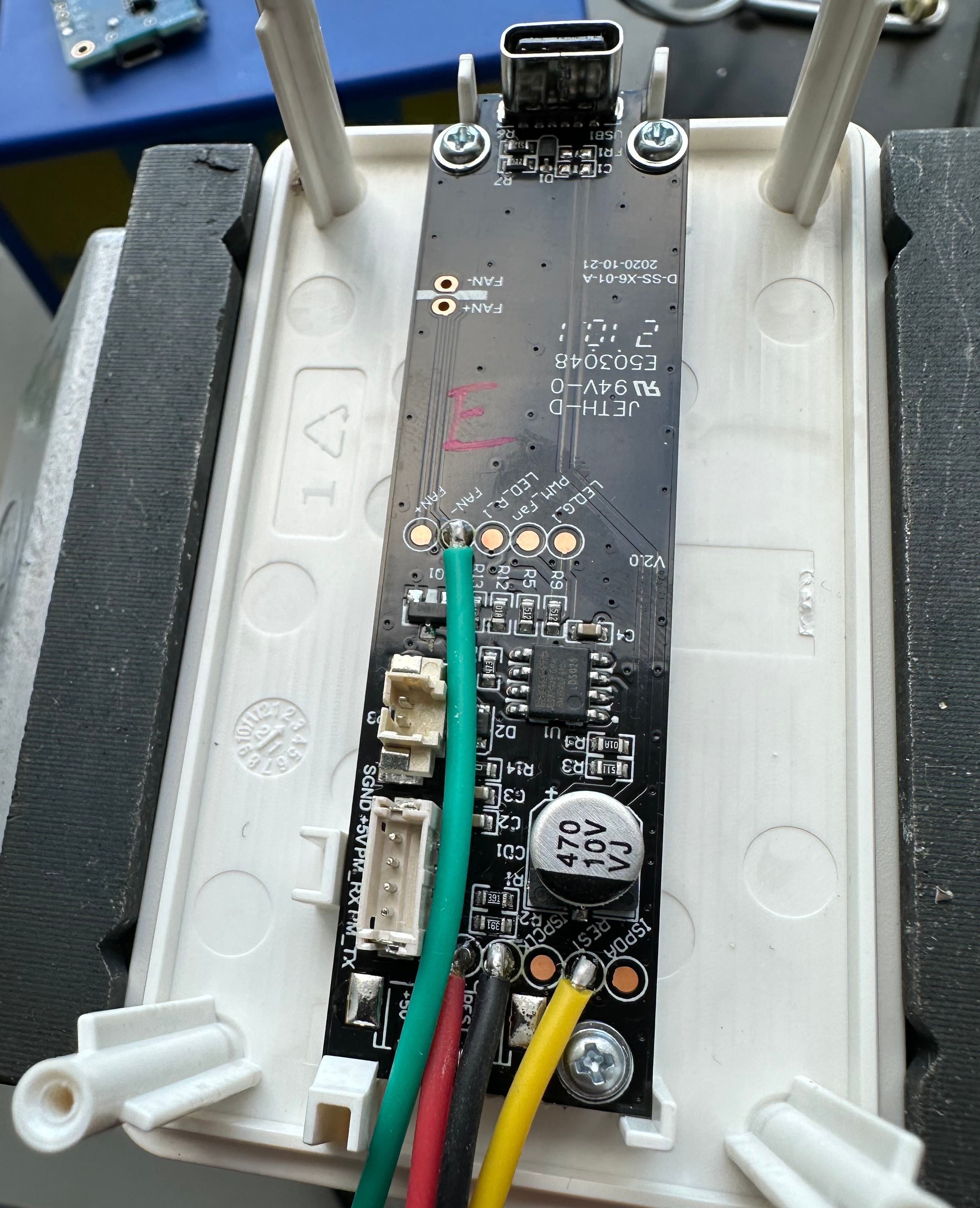 Images shows the main board of an IKEA Vindriktning unit, still attached to the inside of the case lid, with wires soldered to the fan-, +5V, ISPCLK, and REST test pads.